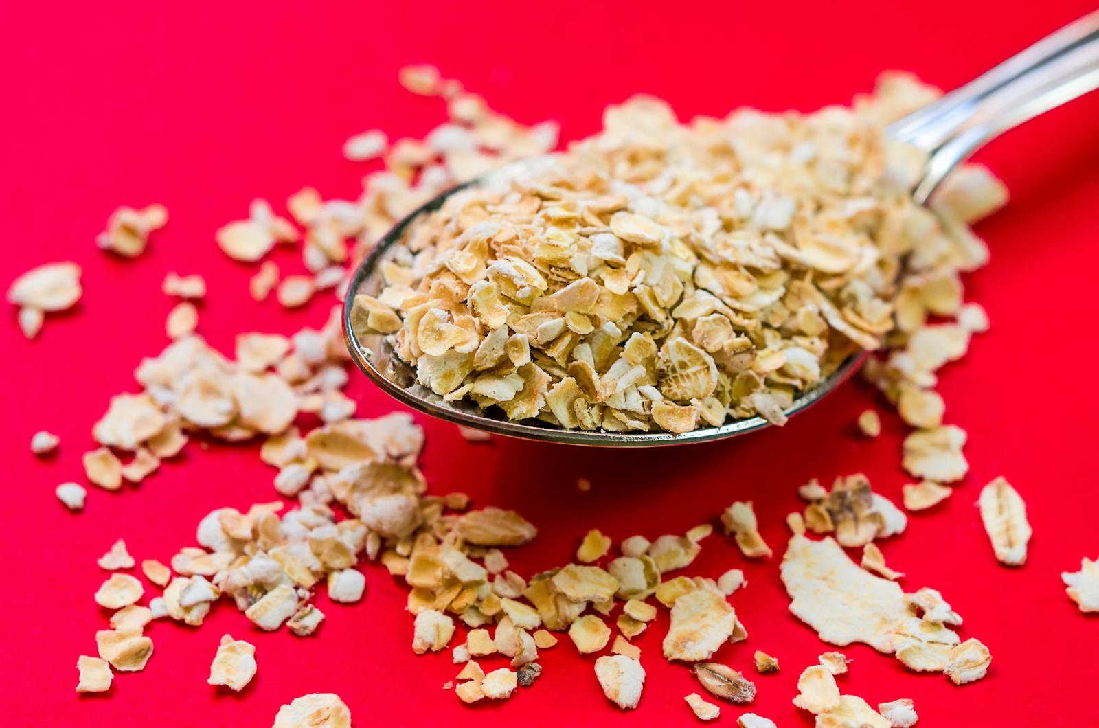 Close-up image of oats scattered on a spoon with vivid red background, perfect for food advertising.
